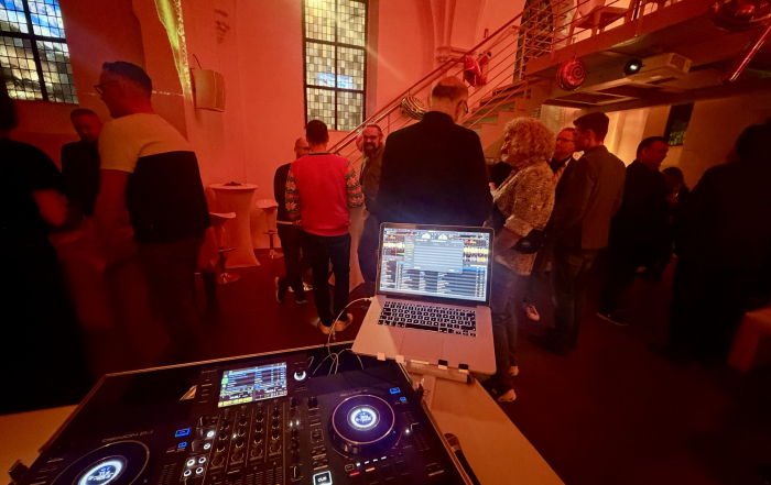 Blick über das DJ Pult auf die Gäste im stimmungsvoll beleuchtetem Raum