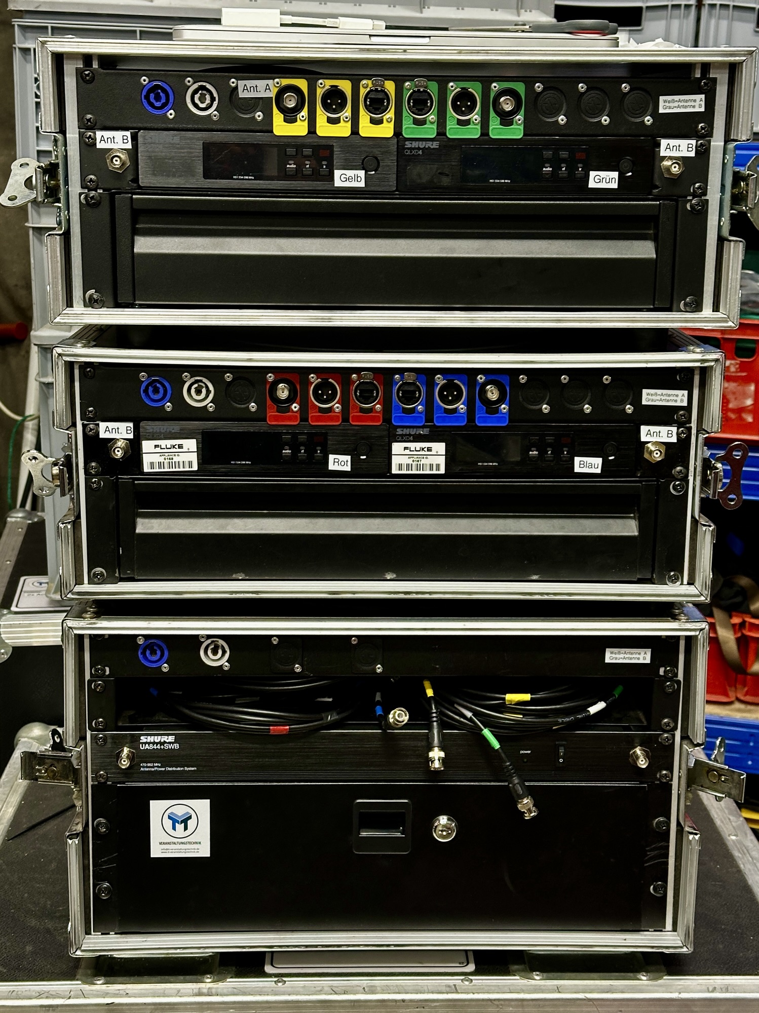 Rack mit mehreren Shure-QLXD4-Funkempfängern in Farbcodierung Gelb, Grün, Rot und Blau sowie einem Shure-Antennenverteiler