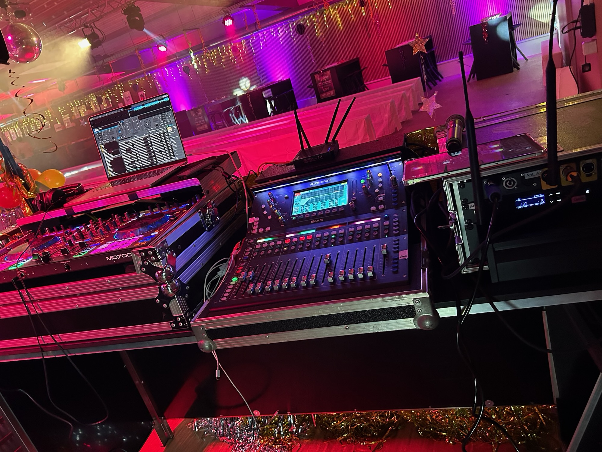 DJ-Pult mit Laptop, Denon-Controller und Allen & Heath SQ-5 Digitalmixer bei einer Party mit bunter Lichterkettenkulisse und Discokugel