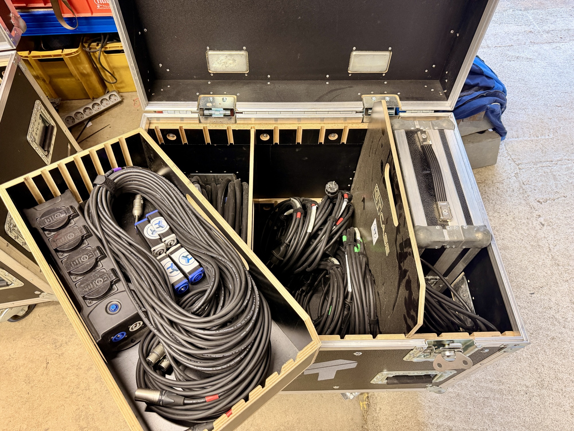 Geöffneter Flightcase mit sauber aufgewickelten XLR- und Lautsprecherkabeln sowie einer Steckdosenleiste mit Powercon-Anschlüssen