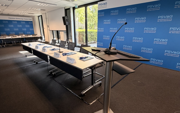 Konferenzraum mit Rednerpult und Mikrofon vor Presswand, davor ein Tisch mit Namensschildern für ein Firmenevent