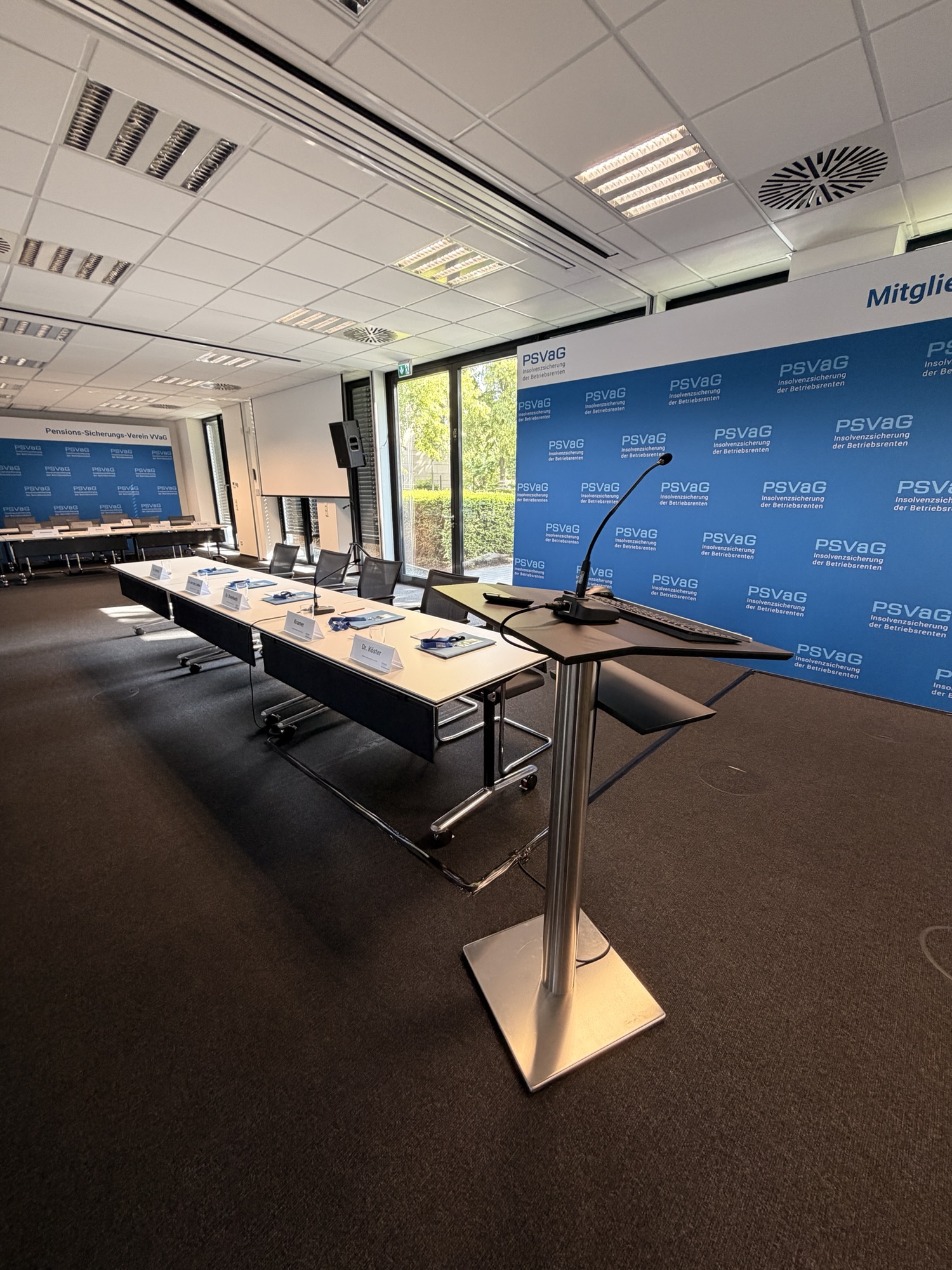 Konferenzraum mit Rednerpult und Mikrofon vor Presswand, davor ein Tisch mit Namensschildern für ein Firmenevent